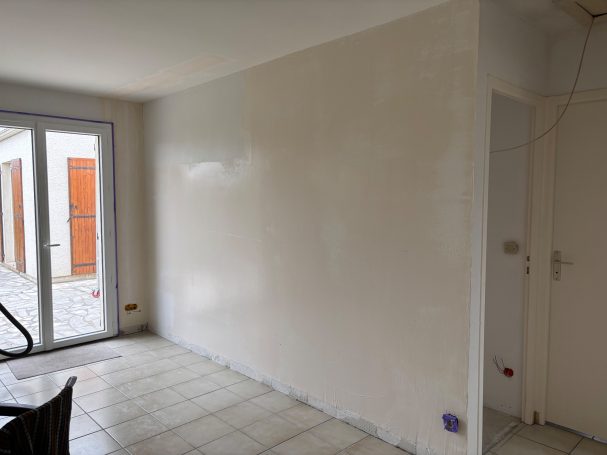 Mur blanc lisse dans une pièce, avec des portes-fenêtres et un coin visible.