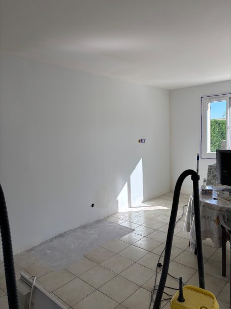 Pièce vide avec mur blanc, sol carrelé et fenêtre éclairant l'espace.