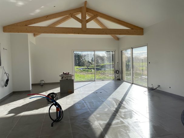 Intérieur d'une pièce lumineuse avec de grandes fenêtres et des poutres en bois au plafond.